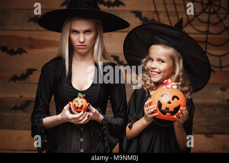 Concetto di Halloween - bella madre caucasica con deluso feeling con piccolo felice figlia godere con Halloween Candy e dolce oltre i pipistrelli e spider web su legno di sfondo per studio. Foto Stock