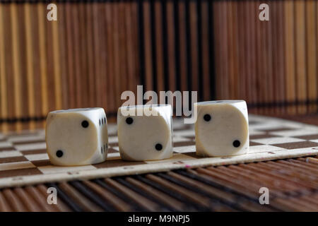 Pila di tre in plastica bianca su plinti in legno marrone sullo sfondo della scheda. Sei lati cubo con punti neri. Numero 2 Foto Stock