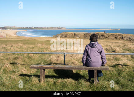 Donna seduta guardando attraverso il Tyne estuario da South Shields verso Tynemouth, North East England, Regno Unito Foto Stock