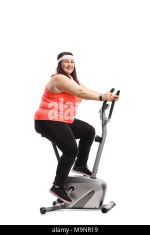 Il sovrappeso donna esercita su una bicicletta stazionaria e guardando la telecamera isolata su sfondo bianco Foto Stock