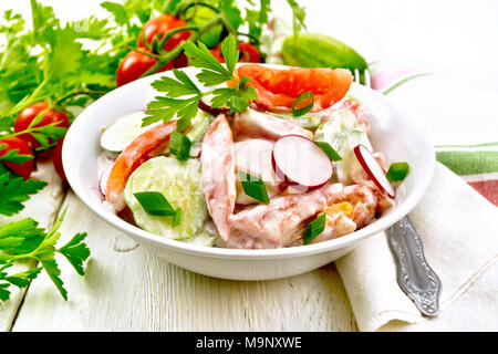 Insalata di pomodori freschi, cetrioli e ravanelli con i cipollotti e il prezzemolo, aromatizzata con la maionese e la panna acida in una ciotola, asciugamano e forcella su un w Foto Stock