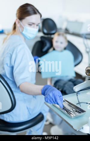 Piacevole dentista femmina selezionando strumento necessario Foto Stock