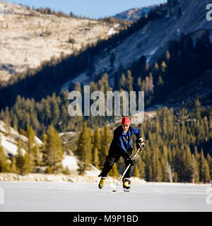 Basso angolo vista frontale di un pattinatore su ghiaccio la riproduzione di hockey su ghiaccio su una neve libera, congelati Tenaya Lake nel Parco Nazionale di Yosemite. Foto Stock