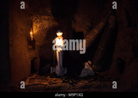 Sacerdote copto a lume di candela nella chiesa rupestre, Lalibela, Etiopia Foto Stock