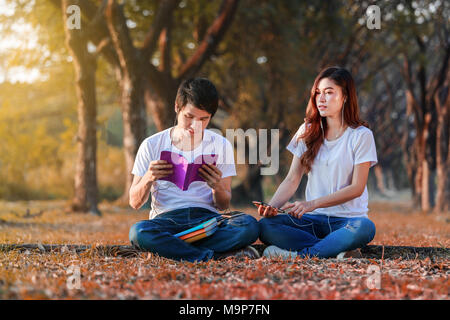 Coppia giovane leggendo un libro e ascoltando la musica con gli auricolari nel parco Foto Stock