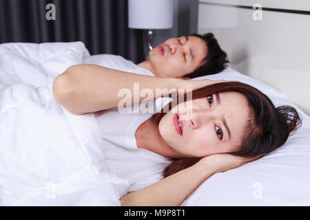 Infastiditi moglie bloccando le sue orecchie dal rumore del marito il russamento in camera da letto Foto Stock
