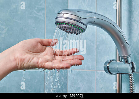 Controlli a mano l'acqua che fluisce dalla doccia, fissata nel supporto in bagno con piastrelle blu. Foto Stock