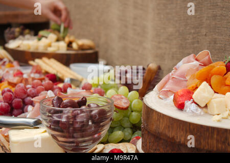 Una luminosa e colorata selezione di frutta, formaggi, salse, salumi e cracker sparsi in una bella lastra di legno. Foto Stock