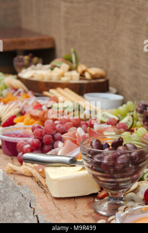 Una luminosa e colorata selezione di frutta, formaggi, salse, salumi e cracker sparsi in una bella lastra di legno. Foto Stock