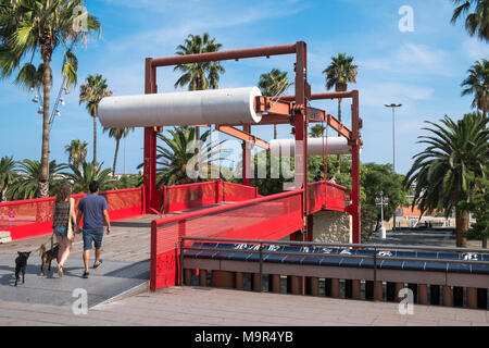 Una coppia e i loro cani a piedi tra il Passeig de Colom e le molle de la Fusta su un dipinto luminosamente ponte pedonale spanning trafficata Ronda de Foto Stock