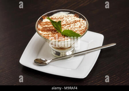 Tiramisù Torta di crema dessert in vetro con foglie di menta nero su sfondo di legno Foto Stock