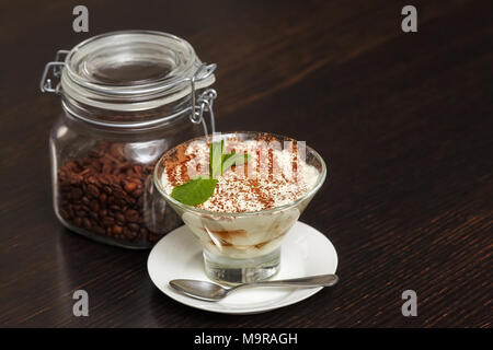 Tiramisù Torta di crema dessert in vetro con foglie di menta e chicchi di caffè nero su sfondo di legno Foto Stock