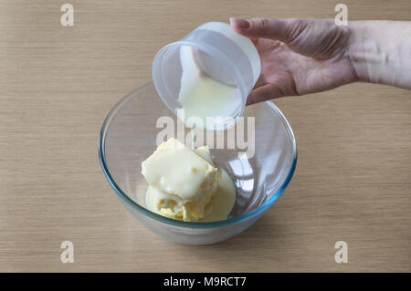 Aggiunta di ingredienti di latte condensato e il burro nel recipiente per la cottura di crema di burro in conformità con la ricetta casalinga Foto Stock