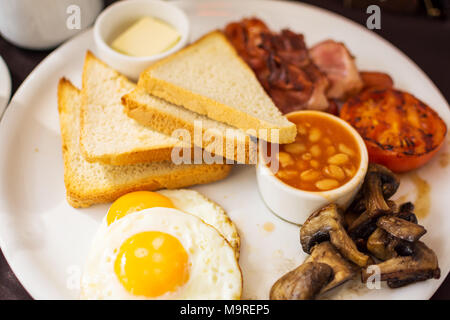 Tradizionale prima colazione inglese con sunny-side-up uova fritte, pancetta, salsicce, fagioli in salsa di pomodoro, toast, pomodori fritti e funghi. Foto Stock