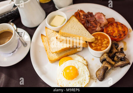 Tradizionale prima colazione inglese con sunny-side-up uova fritte, pancetta, salsicce, fagioli in salsa di pomodoro, toast, pomodori fritti e funghi. Foto Stock