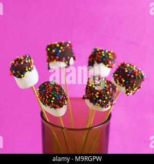 Marshmallows su una stick su sfondo rosa. vetrate con cioccolato e granelli colorati. Foto Stock