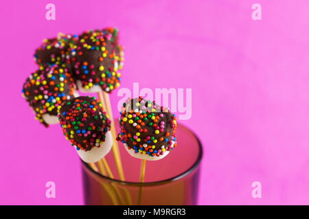 Marshmallows su una stick su sfondo rosa. vetrate con cioccolato e granelli colorati. Foto Stock