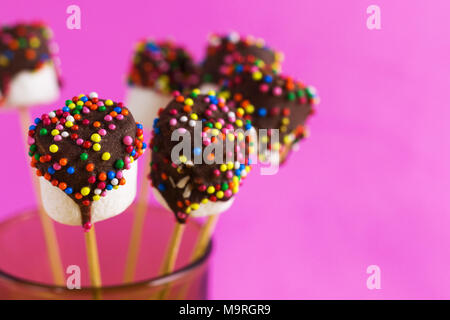 Marshmallows su una stick su sfondo rosa. vetrate con cioccolato e granelli colorati. Foto Stock