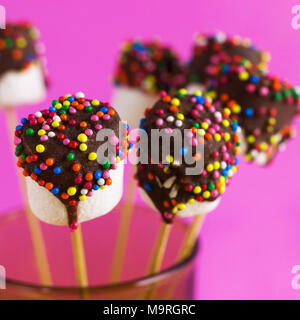 Marshmallows su una stick su sfondo rosa. vetrate con cioccolato e granelli colorati. Foto Stock