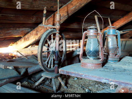 Vintage russo casalinghi. Stilllife. Vecchia ruota di filatura e di lampade a cherosene in un polveroso garret nella casa di campagna. Messa a fuoco selettiva. Foto Stock