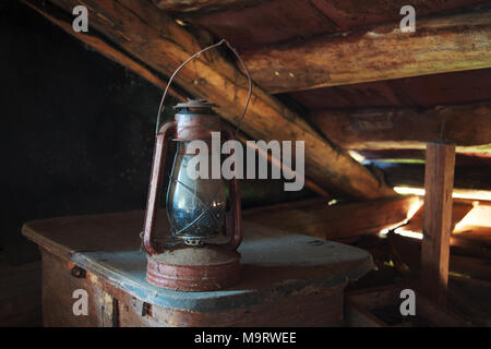 Rarità polverosa lampada a kerosene sorge sul tronco vecchio sotto il soffitto in un vecchio rustico mansarda, il fuoco selettivo, spazio per il testo Foto Stock