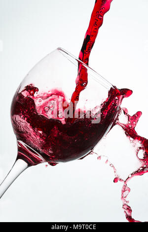 Chiusura del versamento con fuoriuscite di vino rosso su un vetro contro uno sfondo bianco Foto Stock