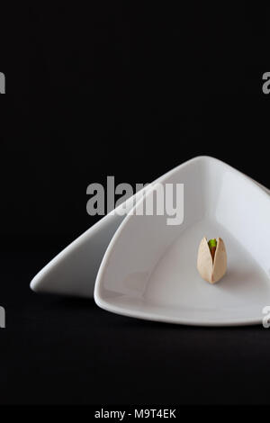 Bianco triangolare di coppe in ceramica con pistacchio su sfondo nero. Cibo scure della fotografia. Foto Stock