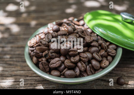 I chicchi di caffè in tazza verde su uno sfondo di legno vecchio con la luce solare Foto Stock