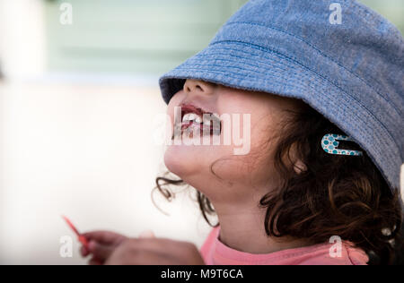 Bambina mangia un gelato mentre si nasconde i suoi occhi sotto il cappello Foto Stock