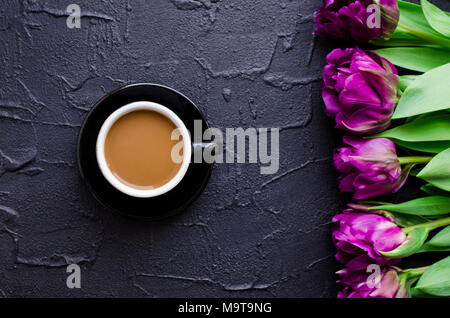 Tazza di caffè con latte e bouquet di tulipani ultravioletta su sfondo nero. La colazione sulla festa della mamma, San Valentino o Womens giorno. Mornin romantica Foto Stock