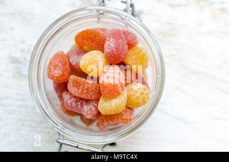 Vitamine gummy nel vasetto di vetro bianco su sfondo di legno. Caramelle multivitaminico in forma di differenti specie di frutta. Supplemento nutrizionale concetto. Parte superiore Foto Stock