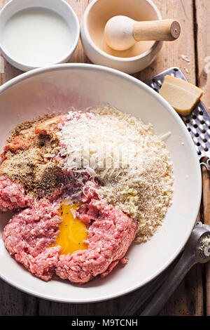 Le polpette di carne gli ingredienti nel recipiente. Carne di maiale tritata, condimento, pangrattato, tuorlo d'uovo, il parmigiano. Foto Stock