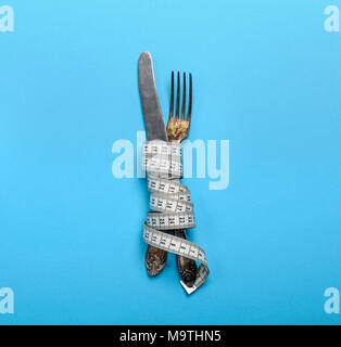 Ferro da stiro forchetta e coltello avvolto in un nastro di misurazione su uno sfondo blu, vista dall'alto Foto Stock