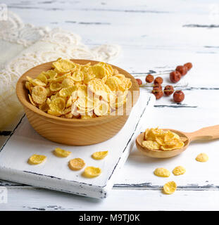 Fiocchi di mais in una ciotola di legno su una lavagna bianca, accanto ad un cucchiaio colmo di cereali, spazio vuoto sulla destra Foto Stock