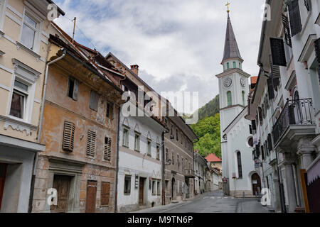 Strada di un piccolo paese di montagna di Slovenia, l'Europa. Squallido case vecchie facciate e tetti. Centro della città e la Chiesa cattolica Foto Stock