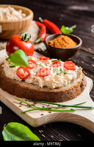Una fetta di pane con il peperoncino cagliata diffusa con cumino in polvere, erba cipollina e basilico Foto Stock