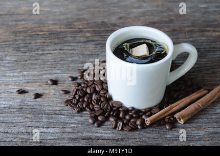 Brown Sugar Cube cadere nella calda tazza di caffè con i chicchi di caffè su uno sfondo di legno Foto Stock