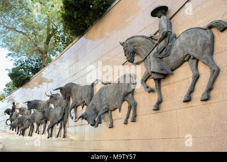 Rilievo bronzeo scultura di tori essendo pilotato da cavalieri a cavallo verso la corrida di Las Ventas, Madrid, Spagna Foto Stock