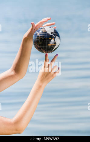 Mani di una giovane donna di bilanciamento di massa sul suo dito - sfera di acqua che mostra vari continenti Foto Stock