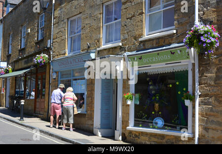 Coppia senior cercando nella finestra di un rivenditore indipendente in strada a buon mercato, Sherborne, Dorset, Inghilterra. Foto Stock