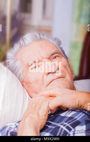 Giovane badante dando aiutando le mani per l'uomo anziano che giace nel male. Foto Stock
