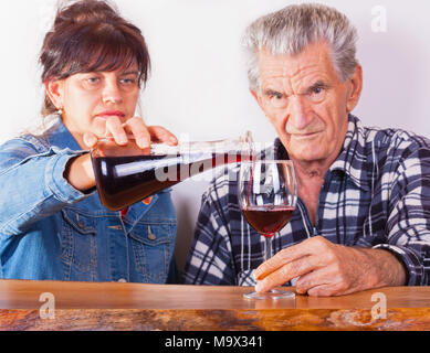 Donna sorridente versando il vino rosso all'anziano padre . Foto Stock