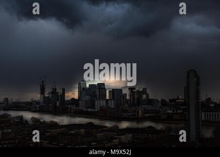 Londra, Regno Unito. 28 marzo, 2018. Meteo REGNO UNITO: l'ultima luce irrompe attraverso una oscura e drammatica del cielo della sera appena prima che il sole tramonta completamente dopo una breve pioggia tempesta su east London compresi Canary Wharf business park di edifici. Credito: Guy Corbishley/Alamy Live News Foto Stock