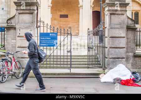 Una persona senza dimora dorme sul marciapiede fuori l'ingresso alla facoltà di storia dell'università nella città di Oxford, Inghilterra, su una giornata invernale Foto Stock