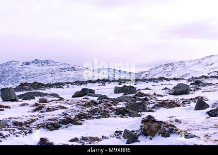 Snowy altopiano con massi di granito in primo piano e le vette delle montagne sullo sfondo Foto Stock