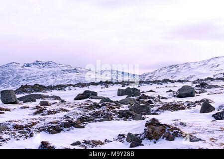 Snowy altopiano con massi di granito in primo piano e le vette delle montagne sullo sfondo Foto Stock