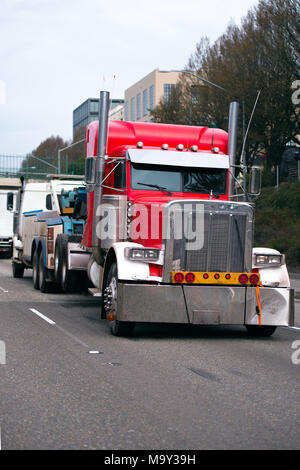 Potente traino di big rig semi traino carrello rotto e danneggiato big rig semi carrello flotta rossa in città il traffico della strada con sicurezza le luci montate Foto Stock