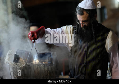 Un ebreo di Haredi immergere gli utensili da cucina in acqua bollente in un processo chiamato Hagalat Kelim (utensili da kashering) per rimuovere i resti di lievito mentre si preparano per la festa ebraica di Pesach (Pasqua) nel quartiere di Mea Shearim, un'enclave ultra-ortodossa in Israele di Gerusalemme occidentale. Gli ebrei trascorrono le settimane prima della Pasqua in una raffica di fuse complete, per rimuovere ogni morsel di cibi lievitati che sono proibiti nella festa ebraica della Pasqua. Foto Stock