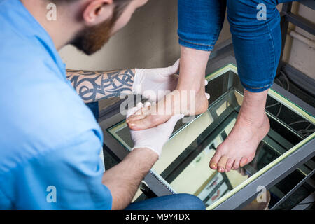 Le mani di un giovane medico ortopedico conduce la diagnostica, piede prova del piede di una donna, per la fabbricazione dei singoli, sottopiedi ortopedici. Foto Stock