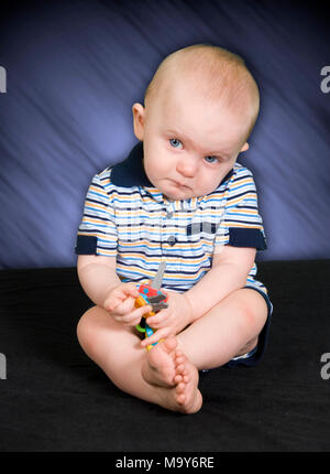 Triste 10 mesi Baby Boy giocando con il giocattolo Foto Stock